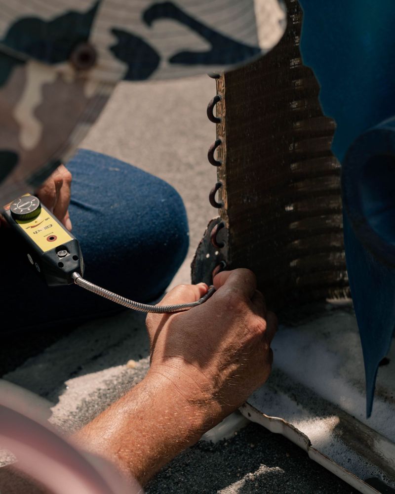 Technician checking an AC coil with a leak detector (stock photo)